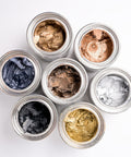 Assorted metallic waxes in small round containers on a white background
