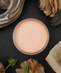 Dixie Belle Paint Apricot Chalk Mineral Paint is the perfect paint for any DIY project!
Open container of Apricot Chalk Mineral Paint staged around the container with ripped pages, tan roses on top of a black background.