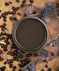 Dixie Belle Paint Coffee Bean Chalk Mineral Paint is the perfect paint for any DIY project!
There is an open paint can that you are looking down on so you only see the brown paint inside. The paint can is sitting on a wood table that has natural sides and is stained in natural and dark wood. There are coffee beans scattered around the paint can. There dried, tan twigs on the table with dried pine cones scattered around and on the twigs.