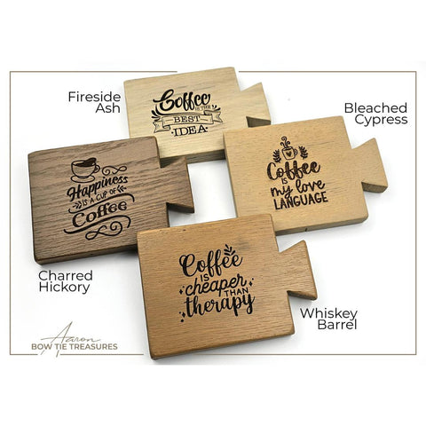 Four wooden coasters with coffee-themed engravings. Designs include "Happiness is a cup of coffee," "Coffee is my love language," "Coffee is cheaper than therapy," and "Coffee is the best idea." Coasters are made from various wood types.