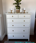 White dresser with six drawers and gold knobs, topped with a potted plant and two white candles in gold holders, standing against a light-colored wall with "Creative Moments" text in the bottom right corner.