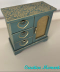 Small blue jewelry box with gold patterns and accents on a light background