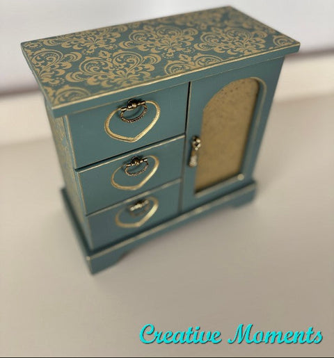 Small blue jewelry box with gold patterns and accents on a light background
