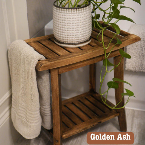Wooden bathroom stand with a potted plant and draped towel on top, and another shelf below. The pot has a white textured design and the plant has trailing green vines. The text "Golden Ash" is in the corner.