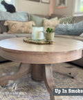 A wooden round coffee table on a patterned rug, holding a tray with a candle and small plant. A cat sits on the sofa in the background. Text reads "Up In Smoke," with logos for Leah Kendrick Design.