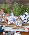 Decorative stars with 'home of the brave' and 'USA' text, surrounded by greenery on a wooden surface.