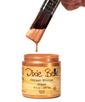 Copper-colored glaze with a brush dipping into it, labeled 'Dixie Belle Copper Bronze Glaze'.