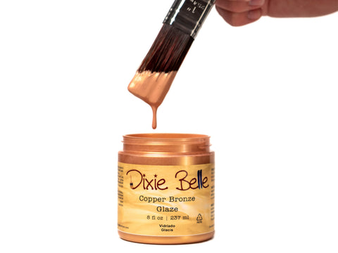 Copper-colored glaze with a brush dipping into it, labeled 'Dixie Belle Copper Bronze Glaze'.