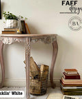 A vintage-style curved table with ornate legs is against a light wall. It holds a plant, books, and a lit candle. A wire basket with wood logs and scattered books surround the table. Text reads "Picklin' White" and "FAFF designs.