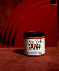 A jar of Dixie Belle Prime Start stands on a red surface with abstract, curved red panels in the background, all under dramatic lighting.