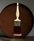 Paint brush with wooden handle and red bristle head floating in front of a dark brown circular platform.