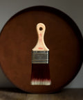 Miini paint brush with wooden handle and metal ferrule in front of a wooden surface.