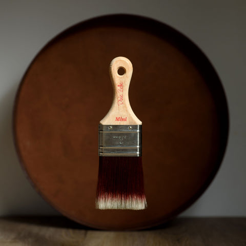 Miini paint brush with wooden handle and metal ferrule in front of a wooden surface.