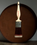 Paint brush with wooden handle and red bristle head floating in front of a dark brown circular platform.