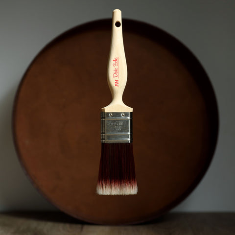 Paint brush with wooden handle and red bristle head floating in front of a dark brown circular platform.