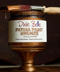 Jar of Dixie Belle Patina Paint Bronze with a brush on a dark background