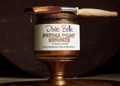 Jar of Dixie Belle Patina Paint Bronze with a brush on a dark background