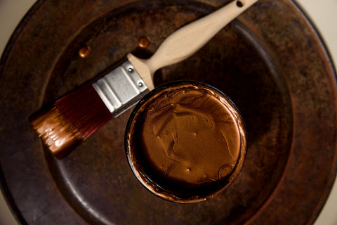 Paintbrush with bronze metallic paint on a round metallic surface