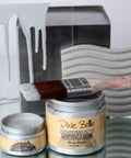 Jars of 'Dixie Belle Moonshine Metallics Silver Bullet' paint with a brush and decorative metal wall art in the background.
