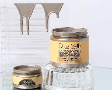 Two jars of Dixie Belle Moonshine Metallic paint on a glass surface with a white background.