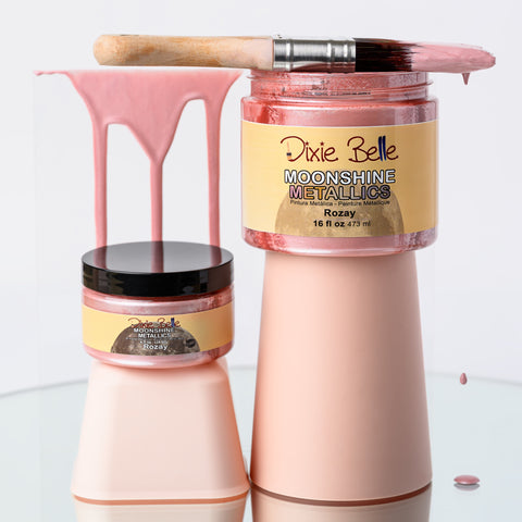 Two bottles of 'Dixie Belle Moonshine Metallic Rozay' with pink and beige colors on a white background.