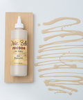A bottle of Dixie Belle VooDoo Gel Stain in Au Naturel, displayed in front of a wooden sample board.