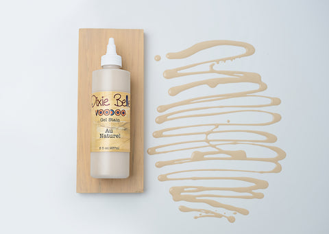 A bottle of Dixie Belle VooDoo Gel Stain in Au Naturel, displayed in front of a wooden sample board.