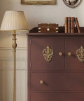 Red-brown dresser with gold accents in a room with framed pictures on the wall.
