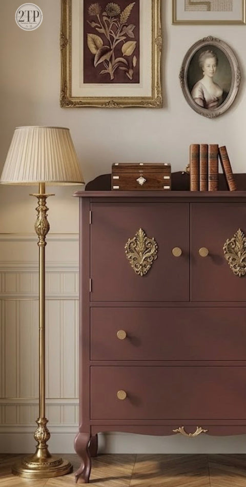 Red-brown dresser with gold accents in a room with framed pictures on the wall.