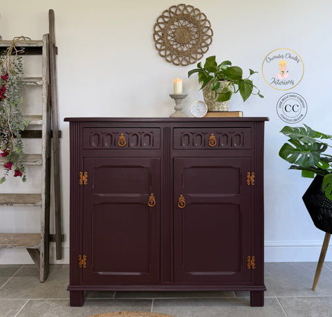 Dark wooden cabinet with decorative elements in a room with plants and a ladder.