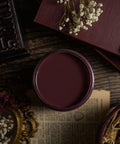 Mauve paint container on a textured surface with dried flowers and a book