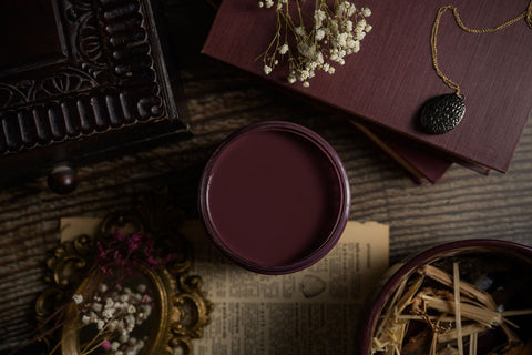 Mauve paint container on a textured surface with dried flowers and a book