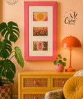 A framed art print with three colorful bohemian-style illustrations is displayed on a peach wall above a yellow cabinet in a styled room setting with a plant, lamp, and chair.