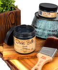 Dixie Belle glaze jars with a brush and wooden block on a white background