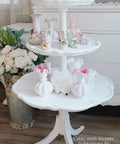 Three-tiered white table with decorative items on a wooden floor, featuring the brand 'Chic and Shabby Furniture by Rebecca'.