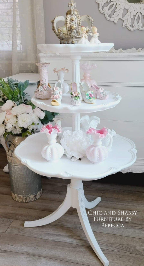 Three-tiered white table with decorative items on a wooden floor, featuring the brand 'Chic and Shabby Furniture by Rebecca'.