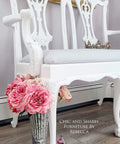 White ornate chair with pink flowers and a mirror in a room setting.