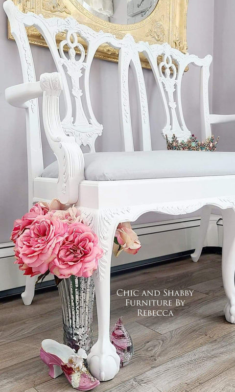 White ornate chair with pink flowers and a mirror in a room setting.