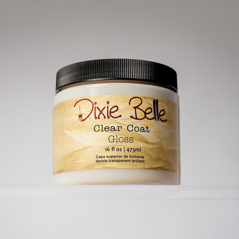 A jar of Dixie Belle Clear Coat Gloss with a black lid and beige label, containing 16 fl oz (473 ml) of product, is displayed against a plain, light background.