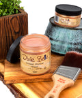 Jars of Dixie Belle glaze and a brush on a wooden surface with a plant in the background