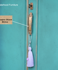 Decorative door handle with tassel on a teal door, featuring 'Sisterhood Furniture' and 'Copper Dixie Shine' text.
