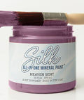 A jar of Silk All-In-One Mineral Paint in the shade Heaven Sent, featuring a lavender-purple paintbrush resting across the open jar on a clean white background.