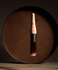 Paint brush with wooden handle and red bristle head floating in front of a dark brown circular platform.