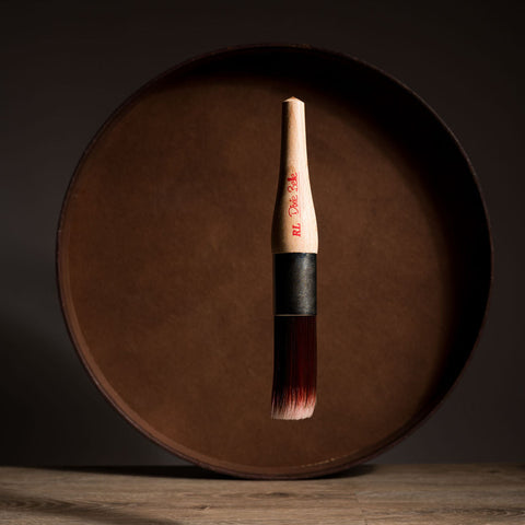 Paint brush with wooden handle and red bristle head floating in front of a dark brown circular platform.