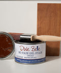 Can of Dixie Belle Cedar gel stain with a wooden stick on a white surface with a gray background
