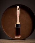 Paint brush with wooden handle and red bristle head floating in front of a dark brown circular platform.