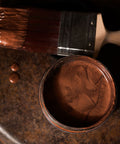 Close-up of a can of copper metallic paint with a brush on a rustic metal surface.