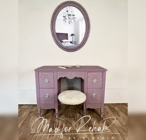 Purple vanity desk with round mirror and stool against a white wall, featuring 'Mad for Rehab by Aleshia' branding.