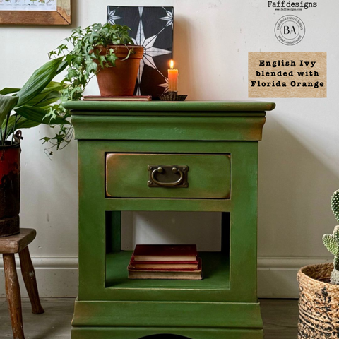 Green wooden side table with a drawer, books, and potted plants in a room setting. Labeled "English Ivy blended with Florida Orange."