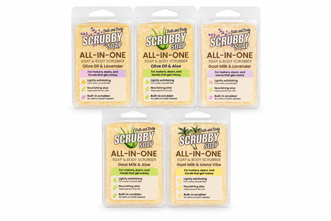 Five packaged Bath and Body Scrubby Soap All-In-One soap bars arranged on a white background. The packages are clear plastic with hanger tabs and display the different scent options: Olive Oil & Lavender, Olive Oil & Aloe, Goat Milk & Lavender, Goat Milk & Aloe, and Goat Milk & Island Vibe.